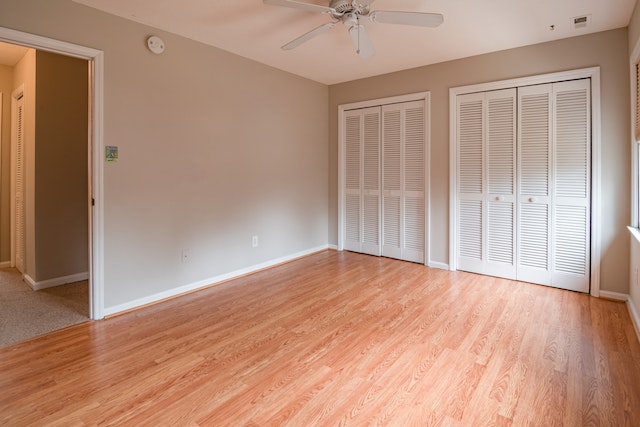 Wide shot of an empty room with light brown wooden floors, beige walls, and white closet doors
